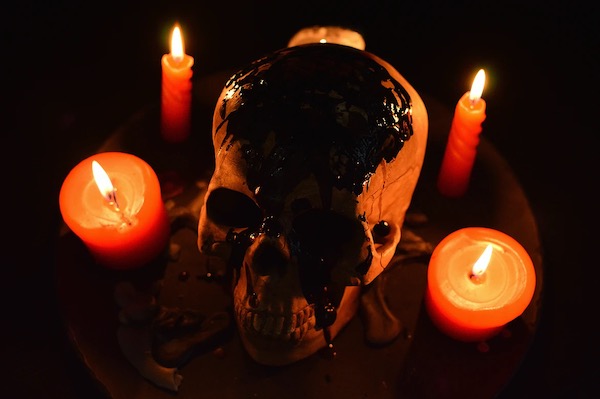 a photograph of a skull surrounded by lit candles, bathed in orange light, against a black background