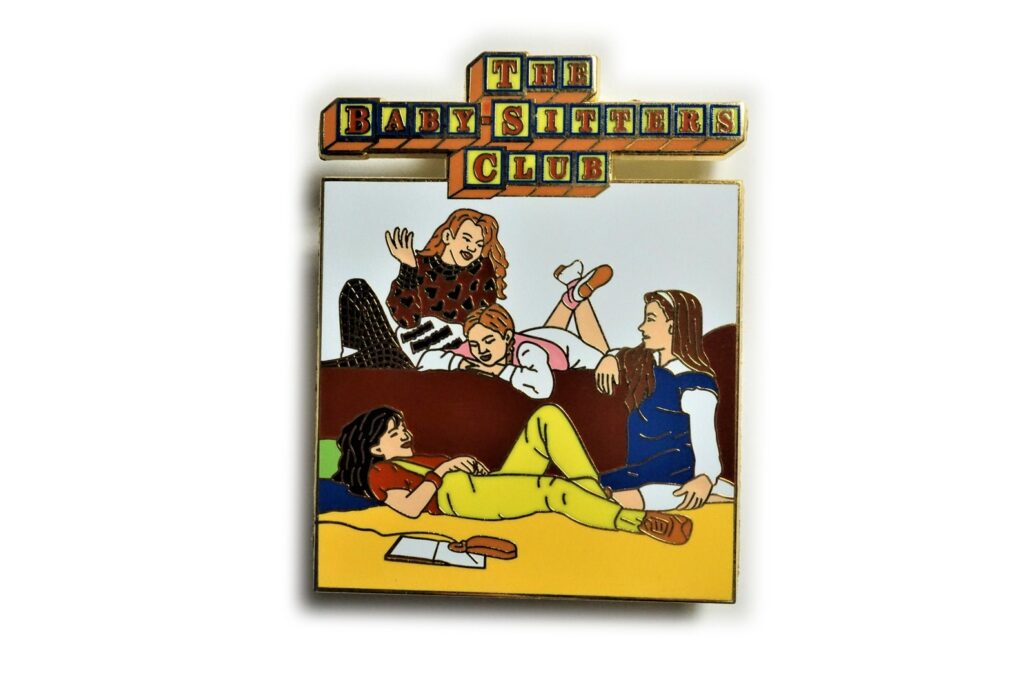 Image of an enamel pin featuring the cover of the first BSC book. 