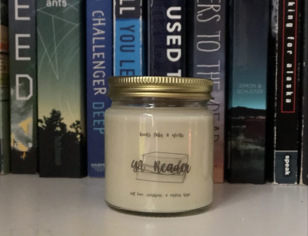 Image of a cream colored candle in front of YA book spines.