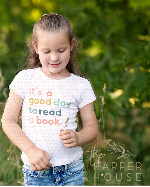 a little girl with jeans and a white shirt that says "it's a good day to read a book" in colorful letters