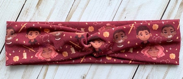A dark red headband with the cartoon-style faces of the main characters of Cemetery Boys repeated on it. So cute!