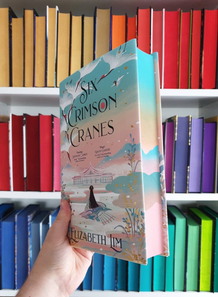 Image of a non-US edition of Six Crimson Cranes, with sprayed edges in a light color palette. 