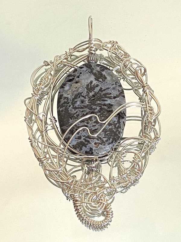 A pendant made of intricate twistings of sterling silver wire around a piece of polished agate.