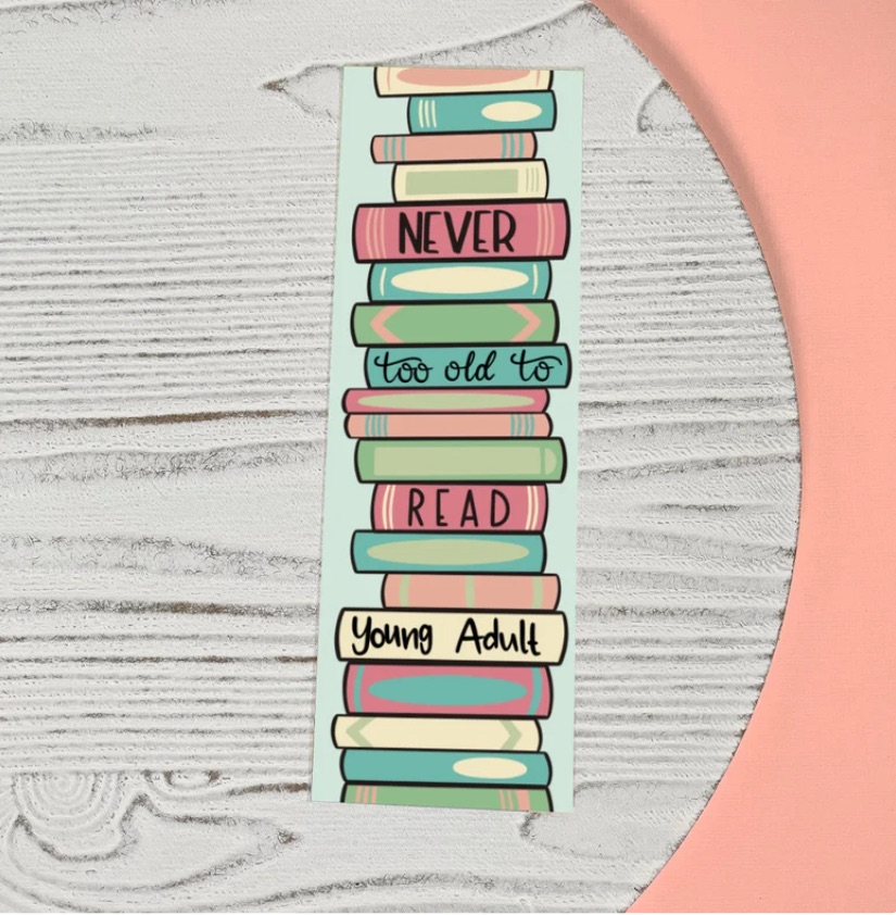 Image of a bookmark on a wood background. The bookmark features a stack of colorful books. The black text on the book spines reads "never too old to read young adult."