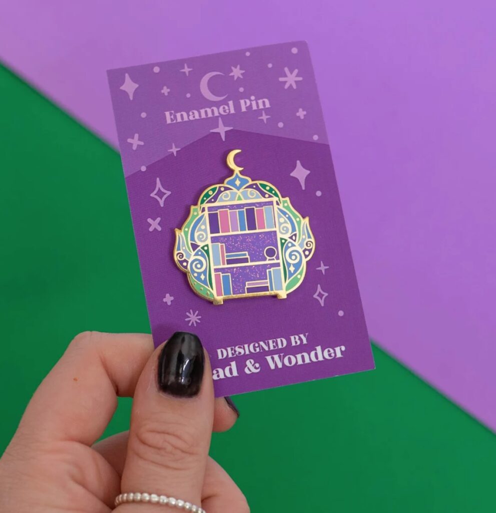 Image of a bookshelf pin. It has a witchy feel to it, with green wisps of smoke surrounding the shelf, and a moon at the very top. It's mostly purples, pinks, and greens. 
