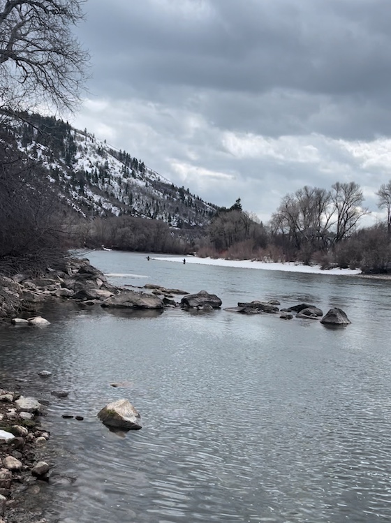 a photo of a mountain creek. The mountains in the background are covered in the snow.