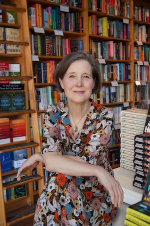 author Ann Patchett sitting with her arms crossed in front of bookshelves in a bookstore